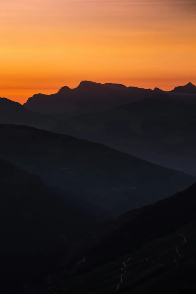 Silhouette de montagnes majestueuses sous un ciel orange vif au lever du soleil.