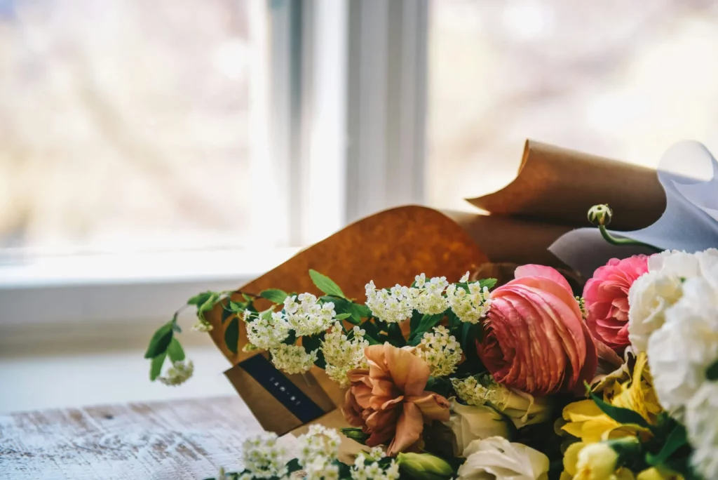 Bouquet de fleurs de ranunculus et de spirea près d'une fenêtre sur une table en bois.